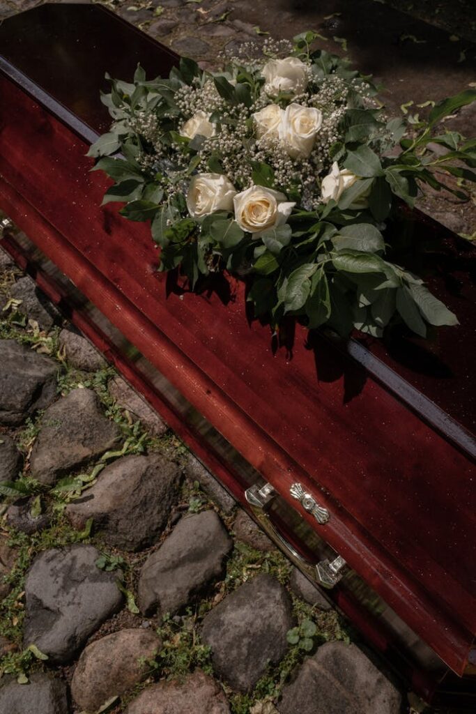 A mahogany coffin adorned with a lush white rose wreath, set in a serene graveyard.